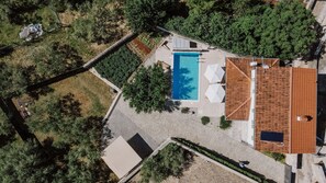 An aerial view of a property with a swimming pool, a covered patio area, and a tiled-roof building.
