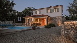 Una villa con fachada de piedra, piscina y zona de patio.