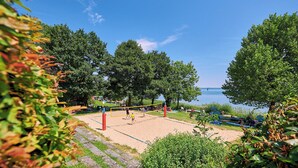 Ein Beachvolleyballfeld mit Netz, umgeben von Bäumen und Blick auf das Wasser.