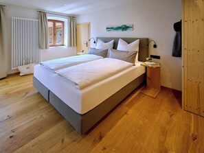 Ein ordentlich bezogenes Bett mit weißen Leinen, ein Nachttisch mit einer Lampe und ein Holzboden.