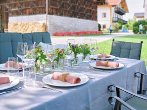Ein Essbereich im Freien mit einem Tisch für vier Personen, ausgestattet mit klarem Glasgeschirr, rosa Servietten und floralen Mittelstücken.