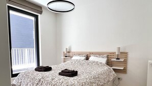 Une chambre moderne avec un grand lit, des lampes de chevet, une tête de lit en bois et une vue sur le balcon extérieur.