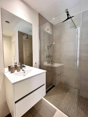 A modern bathroom with a glass-enclosed shower, a white vanity with a mirror, and a tiled floor.