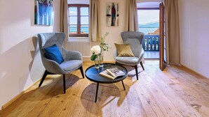 A room with two grey armchairs, a round coffee table, and a view of the sea through a window.