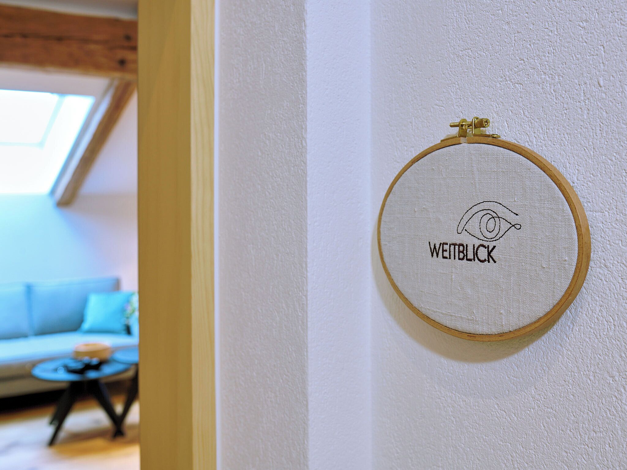 An embroidery hoop with the word "WEITBLICK" on a white wall.