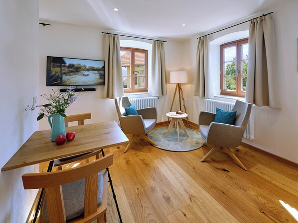 Una sala de estar moderna con una mesa de comedor de madera, dos sillones, una lámpara de pie y un televisor montado en la pared.