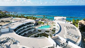 A resort with a central pool, multiple balconies, and a view of the ocean. - LUX 2BD Condo | ONE Mambo Beach 3 by Bocobay (Willemstad)