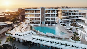 Ett modernt hotell med en central pool, flera balkonger och utomhusområden med sittplatser.