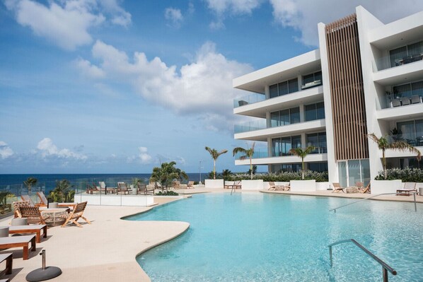 Un hôtel moderne doté d’une piscine, de chaises longues et offrant une vue sur l’océan.