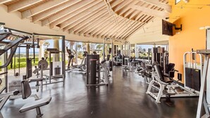 A gym with various exercise equipment, a wooden ceiling, and large windows offering a view of palm trees.