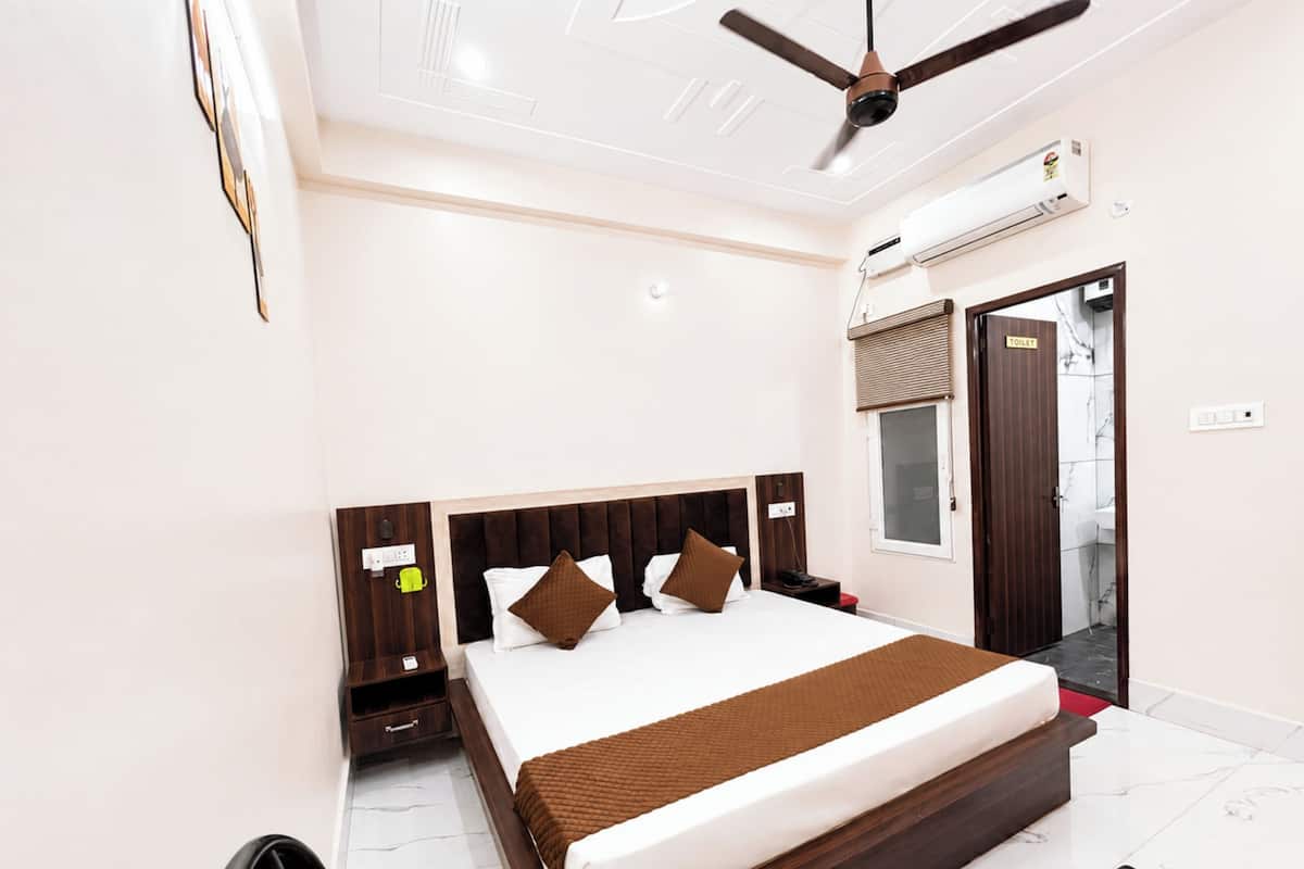 Habitación de hotel con cama, mesita de noche, ventilador de techo, aire acondicionado y vistas al baño.