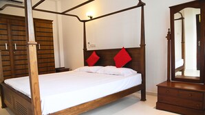 Una cama con dosel de madera, ropa de cama blanca y almohadas rojas, un aparador de madera y un espejo.