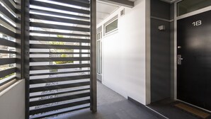 Un couloir avec une porte noire portant l’inscription « 18 », une grille métallique et un mur blanc avec une fenêtre.