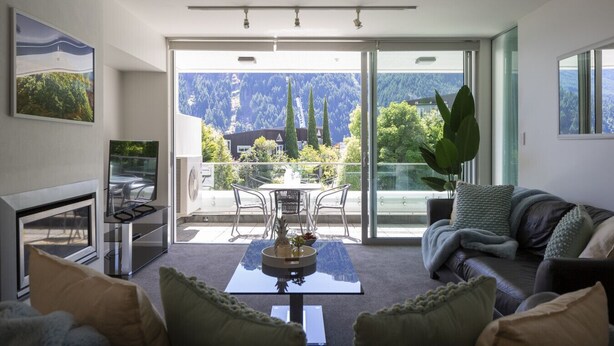 Un salon moderne avec une porte vitrée donnant sur un balcon, une cheminée et une vue sur les montagnes.