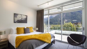 Ein modernes Hotelzimmer mit einem großen Bett, Bergblick und einem Balkon mit einem Sessel.