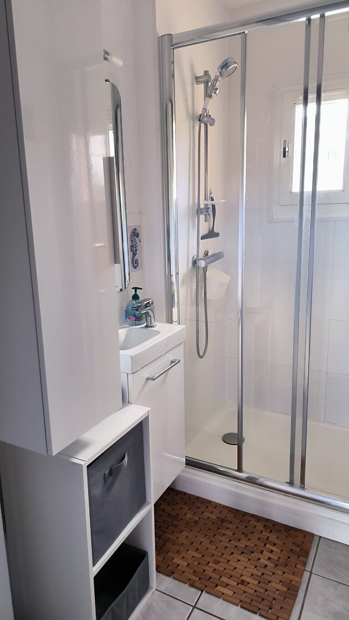 Een moderne badkamer met een douchecabine van glas, een witte wastafel met spiegel en een klein plankje.