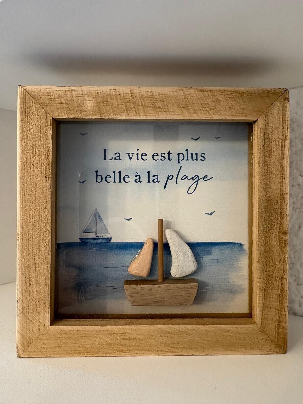 A framed artwork with a sailboat and the text "La vie est plus belle à la plage" (Life is more beautiful at the beach).