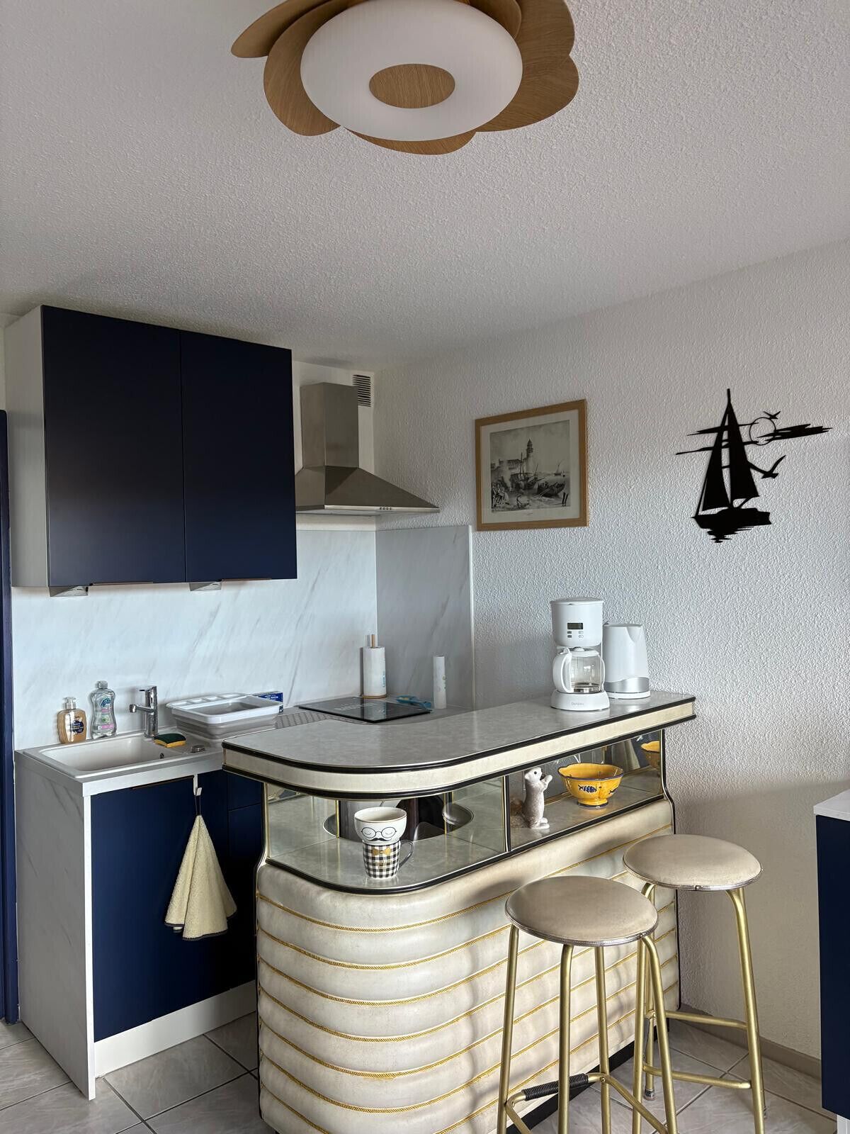 A compact kitchen with a central island, bar stools, and a coffee machine.