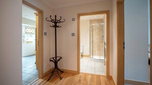 Un pasillo con una lámpara de pie, una puerta de ducha de cristal y vistas a otra habitación con un inodoro.