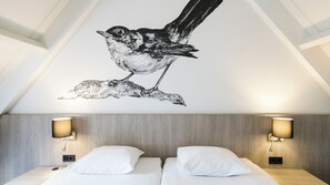 Relax in a stylish room with a unique bird decal, comfortable beds, and ambient lighting.
