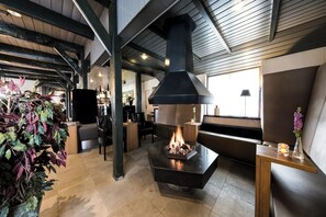 Cozy lounge area with a central fireplace, leather sofas, and a wooden table.