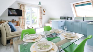 Un coin repas avec une table dressée pour quatre personnes, un canapé, un téléviseur et un espace cuisine équipé de placards et d’un four à micro-ondes.
