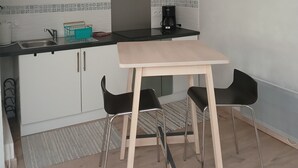 Una cocina moderna con armarios blancos, encimera negra y una cafetera. Hay dos sillas negras y una mesa de madera.