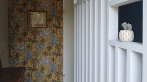 Un pasillo con papel tapiz estampado, un armario de madera, una partición blanca y un candelabro colgante.