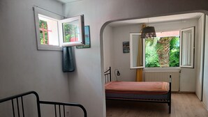 Un dormitorio con cama, una silla, un ventanal con persiana abierta y un radiador.