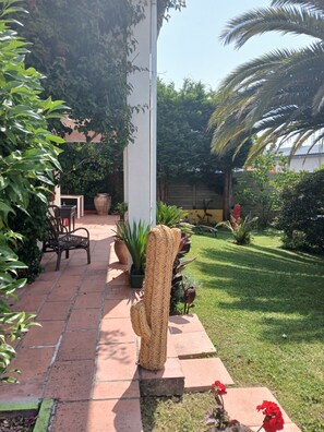 Ein Gartenpfad mit Topfpflanzen, einer Bank und einer dekorativen Gewebestruktur.