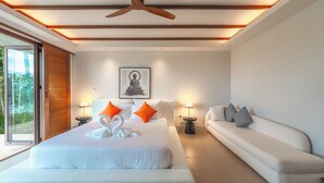 Une chambre d’hôtel moderne avec un grand lit, un canapé, un ventilateur de plafond et une statue de Bouddha accrochée au mur.