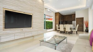 A modern living room with a flat-screen TV, glass coffee table, and a dining area with chairs and a table. - Luxury Pool Villa A14 3BR/8 Persons (Muang Pattaya)