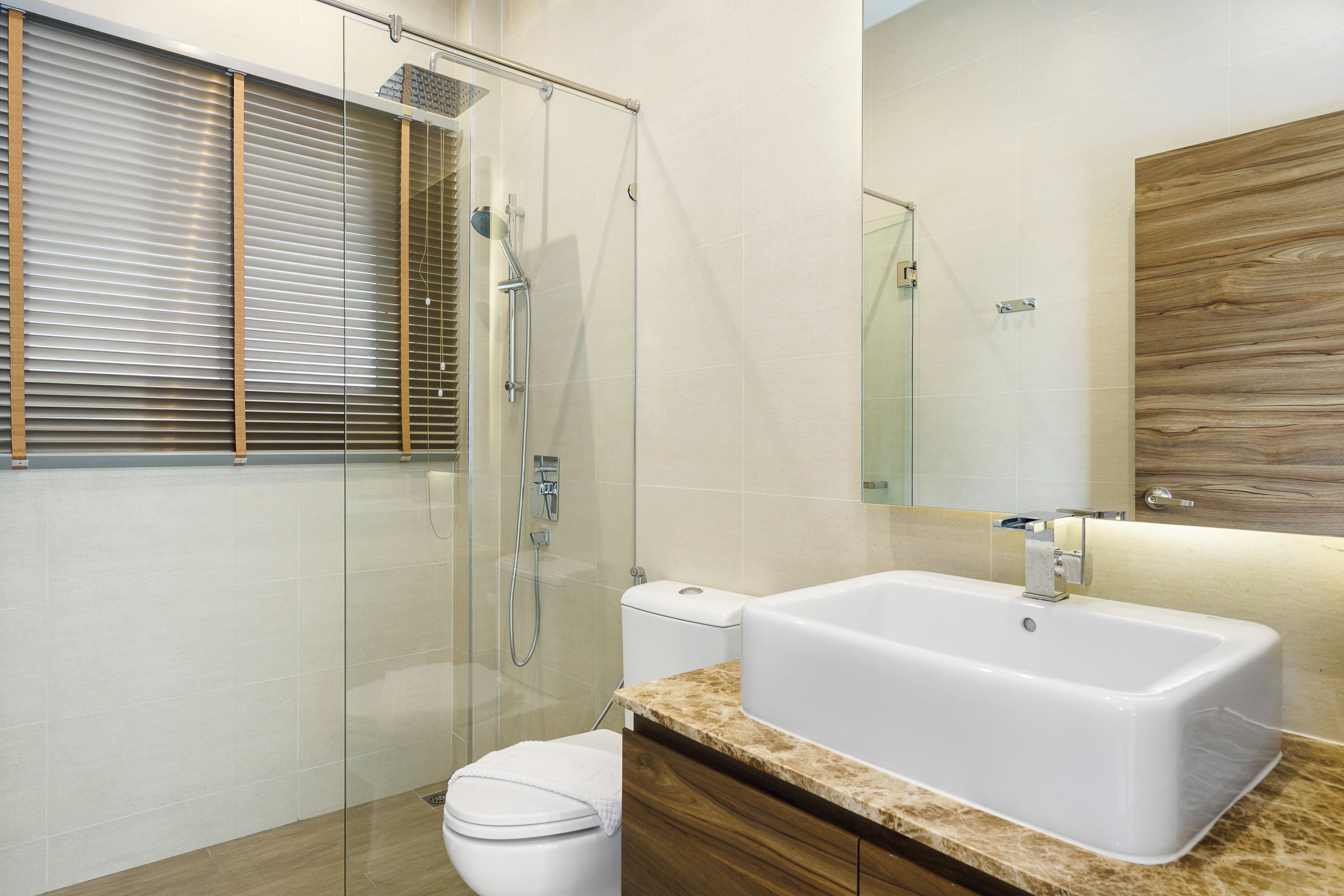 Ein modernes Badezimmer mit einer Duschkabine aus Glas, einer weißen Toilette und einem großzügigen, rechteckigen Waschbecken mit Holzplatte.
