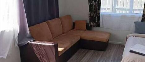 A room with a sectional sofa, a bed, and a window with curtains.