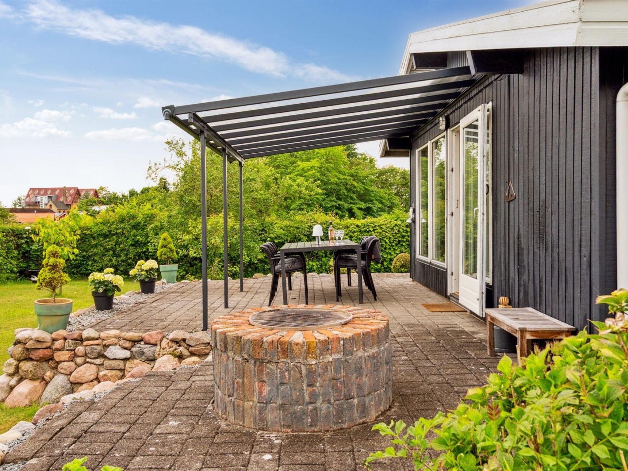 A patio with a brick fire pit, a table and chairs, and a pergola.
