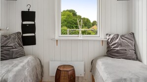 Une chambre avec deux lits, une fenêtre donnant sur un espace verdoyant, un radiateur et un étagère suspendue.
