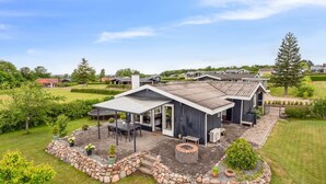 Une maison moderne dotée d’un patio couvert, d’un aménagement paysager en pierre et d’une grande pelouse.
