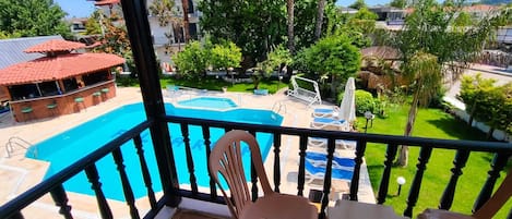 A balcony with a view of a swimming pool, a bar area, and surrounding greenery.