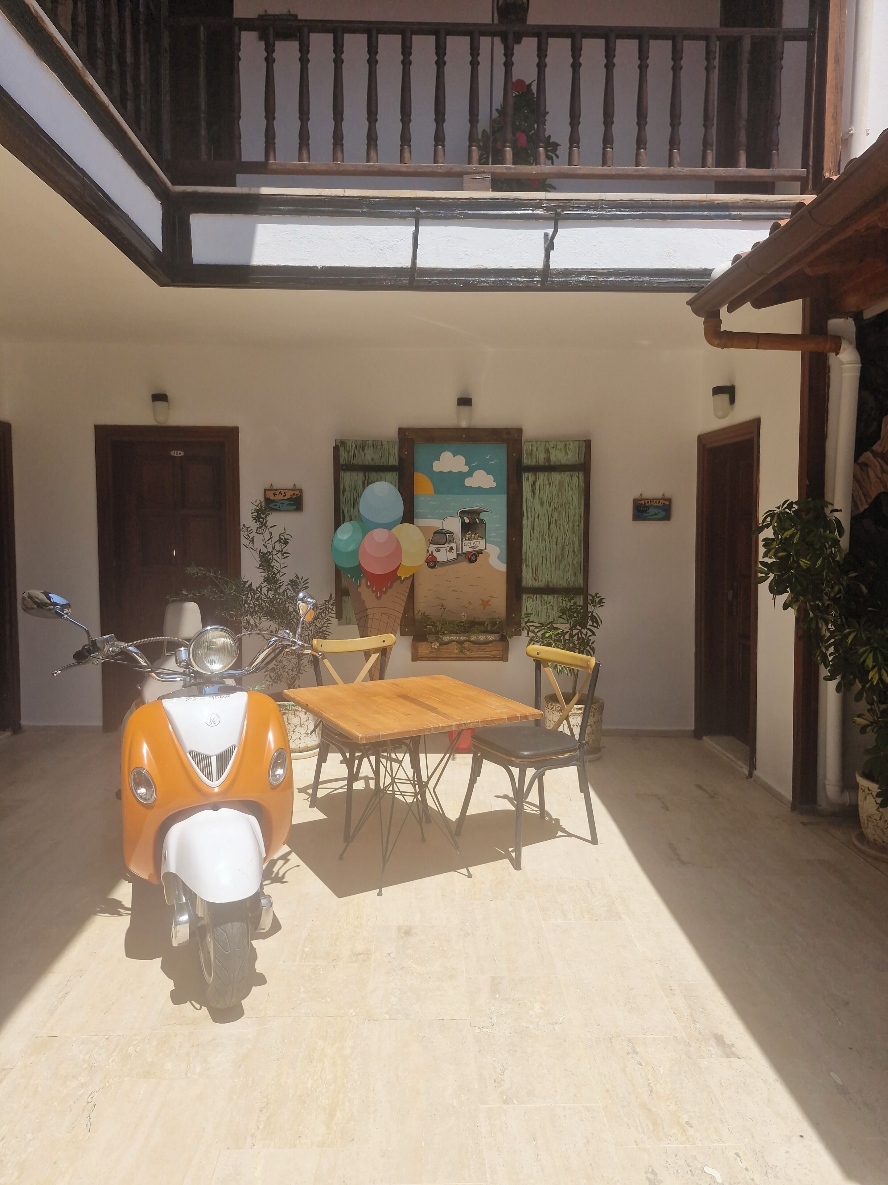 Un espace extérieur abrité comprenant une trottinette, une table, des chaises et un tableau accroché au mur.