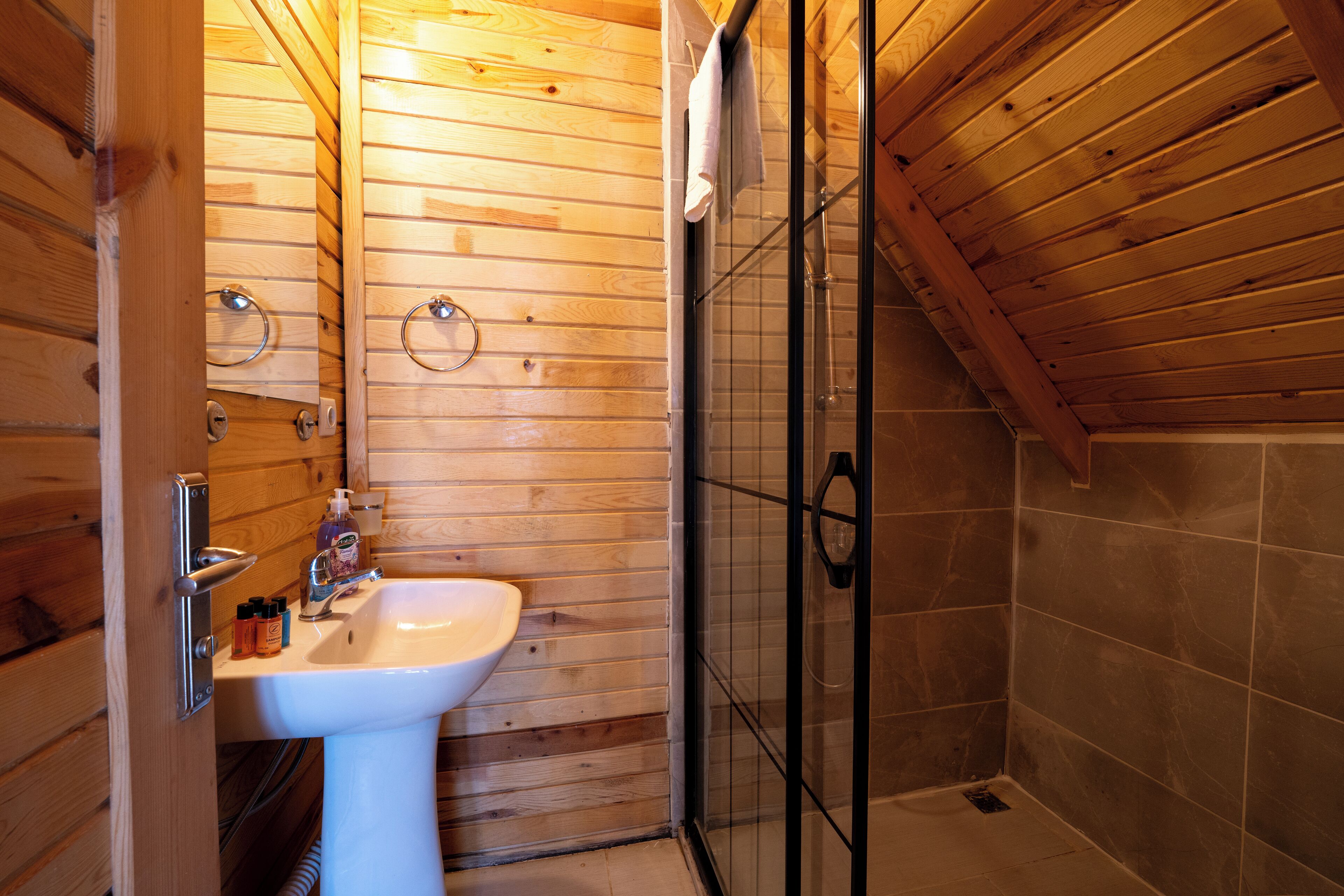 Un baño con detalles de madera, que incluye un lavamanos, jabón de manos y una cabina de ducha con mampara de vidrio.