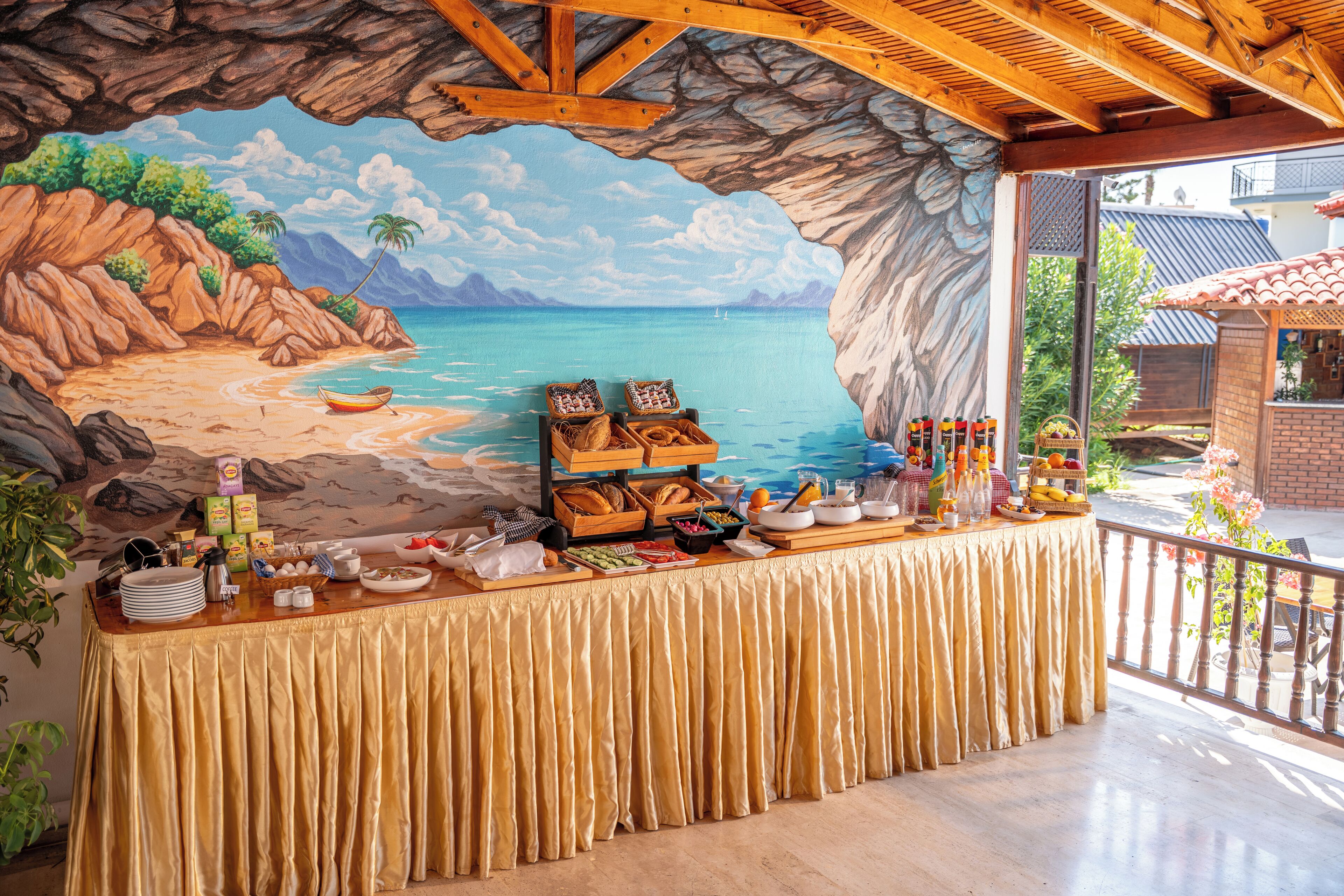 Una mesa de buffet con un mural tropical de fondo, que muestra una escena de playa y una variedad de alimentos.