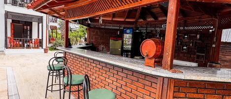An outdoor bar area with brick walls, wooden beams, and green bar stools.