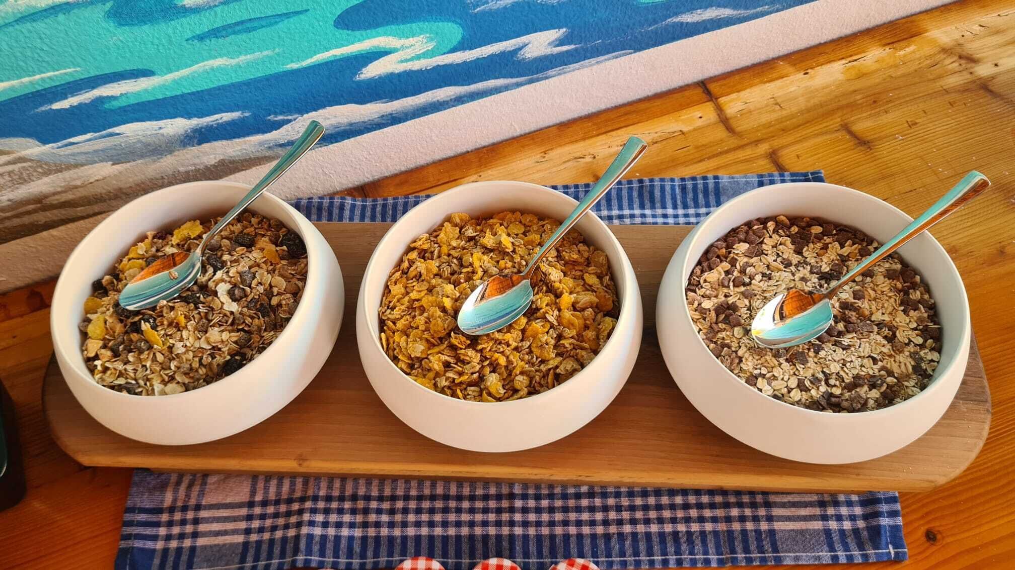 Three bowls of cereal on a wooden board with a blue and white checkered cloth underneath.