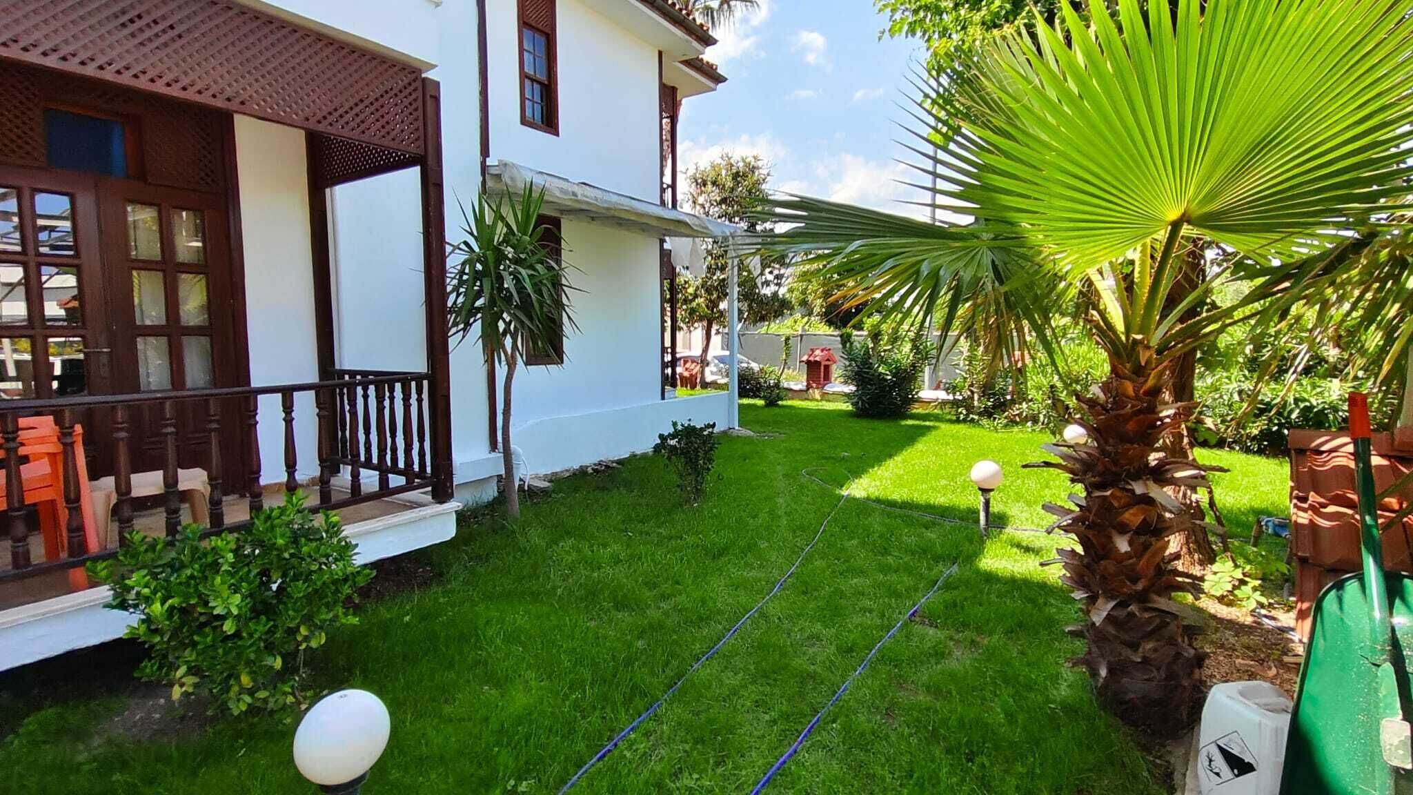 A well-maintained garden with a lawn, a palm tree, and a house with a balcony.