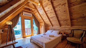 A cozy wooden cabin bedroom with a large bed, a chair, and a view of the outdoors. - Palma Rosa Hotel (Kemer)