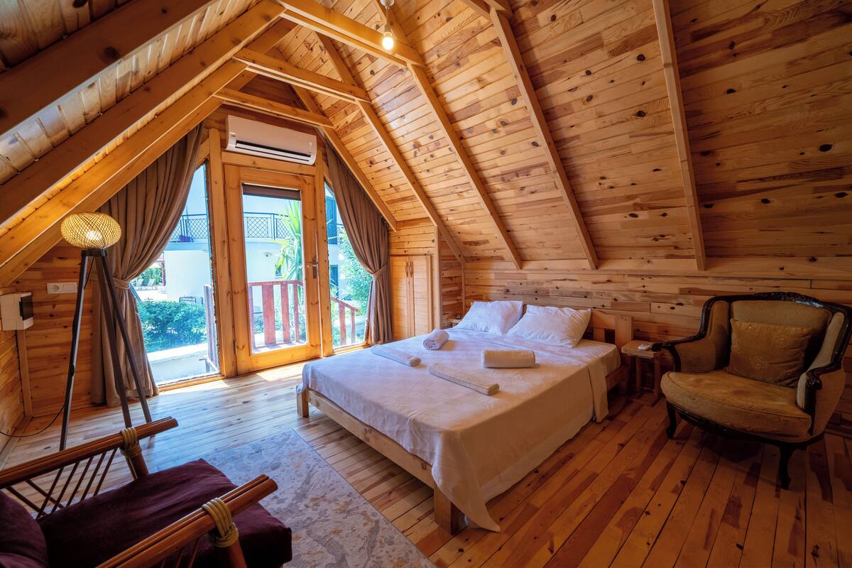 A cozy wooden cabin bedroom with a large bed, a chair, and a view of the outdoors.