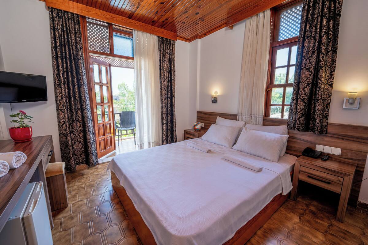 A bedroom with a large bed, wooden headboard, a TV mounted on the wall, and a small table with a red bowl and towels.