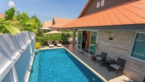 A swimming pool with lounge chairs and a table, surrounded by a brick wall and a covered patio area.