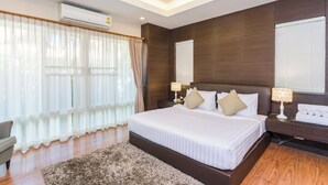 A modern bedroom with a large bed, wooden paneling, a ceiling fan, and a window with curtains.
