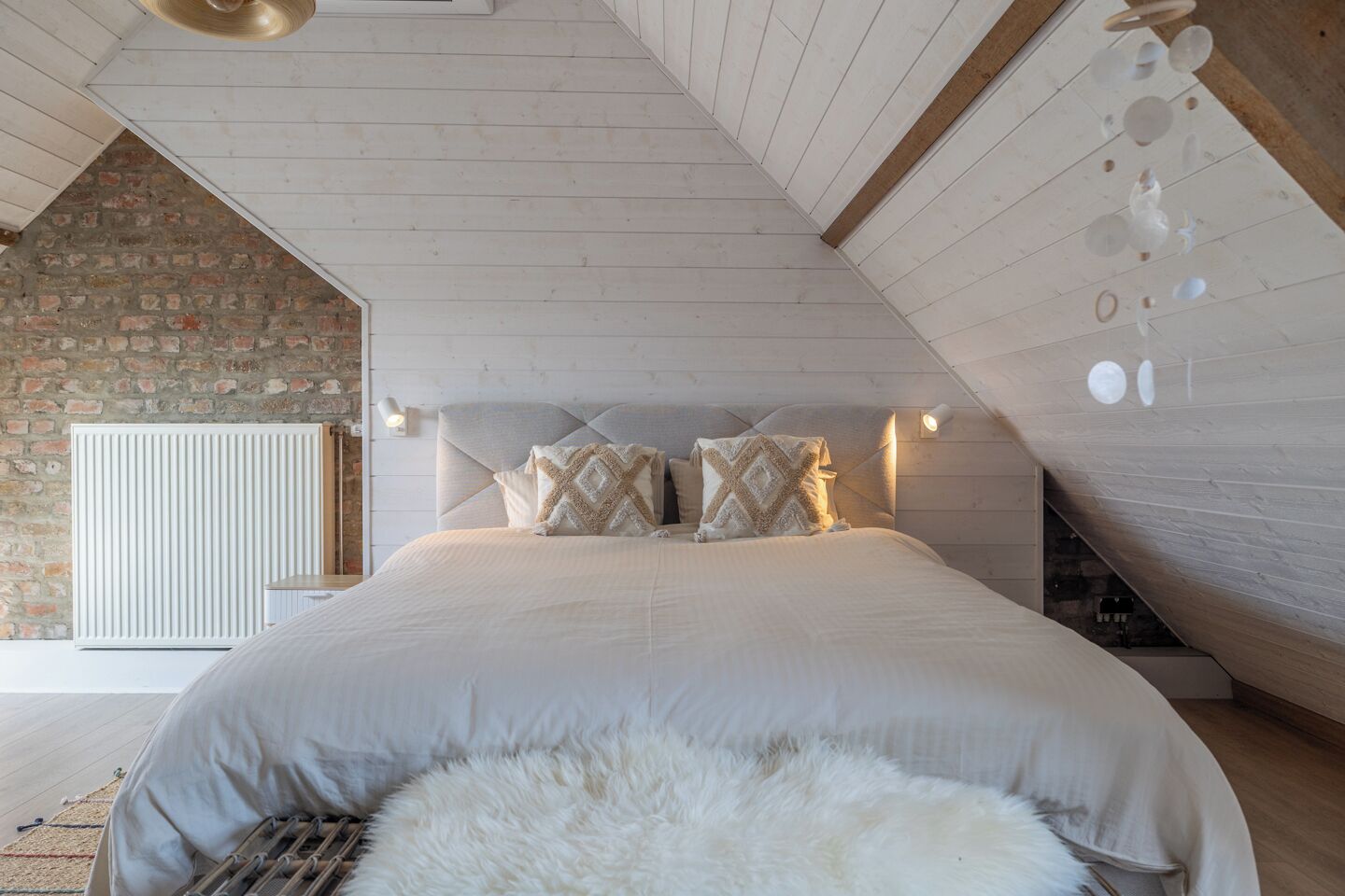Una camera da letto con soffitto spiovente, parete in mattoni, termosifone e letto con cuscini.